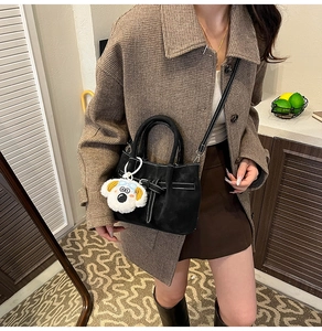 Détail du sac seau en daim noir avec pendentif chien en peluche porté par un mannequin