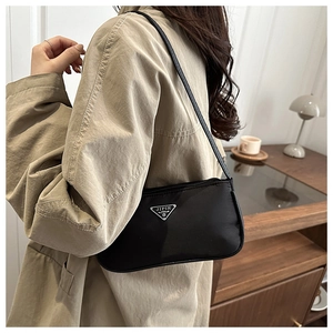 Close-up of minimalist black nylon underarm bag with triangular logo on beige trench coat