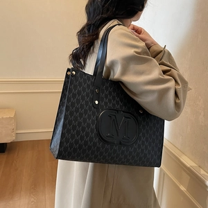 Classic black PU tote bag with M-pattern print and large embossed logo on a model