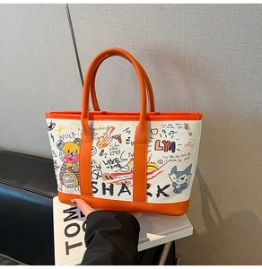Detailed close-up of orange leather handles and street graffiti print on canvas tote bag