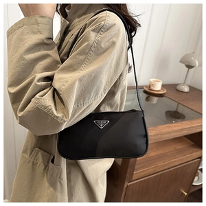 Detail of minimalist black nylon shoulder bag with silver triangle logo on soft interior background