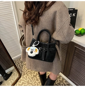 Détail du sac à bandoulière en daim noir avec surpiqûres et breloque chien en peluche
