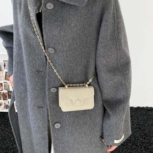 Mini sac carré beige minimaliste avec chaîne dorée sur un manteau en laine grise