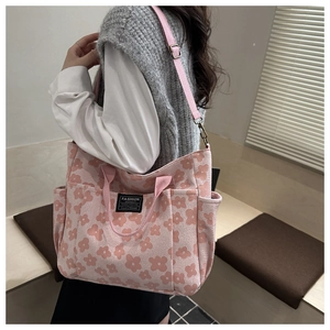Detail of pink floral canvas tote bag featuring a front fashion label and adjustable strap