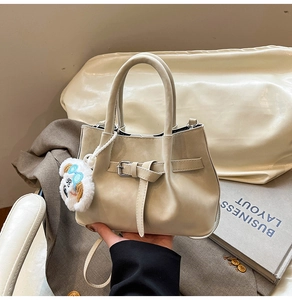 Détail du sac beige en cuir avec boucle et breloque peluche sur une veste de costume