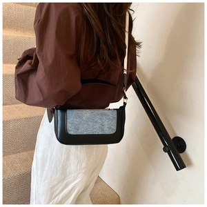 Detail of a minimalist black leather crossbody bag with light blue denim fabric patchwork