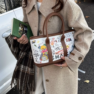 Fashionable graffiti tote bag with brown leather handles styled for winter fashion