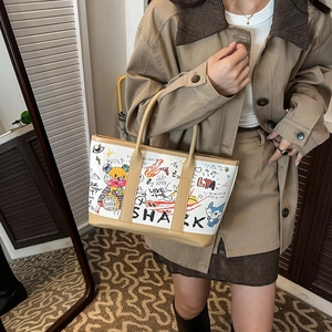 Fashionable tote bag with colorful graffiti art design and brown handles on model