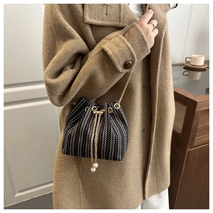 Detail of woven bucket bag with herringbone texture, gold chain and pearl drawstrings