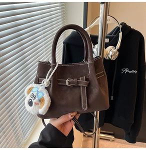 Détail du sac bandoulière en daim marron avec boucle décorative et breloque en peluche