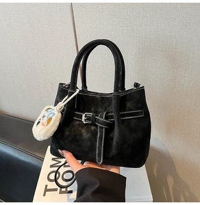 Détail du sac seau noir en daim mat avec surpiqûres blanches et charme en peluche