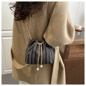 Detail of woven bucket bag with gold chain and pearl tassels worn over a wool coat