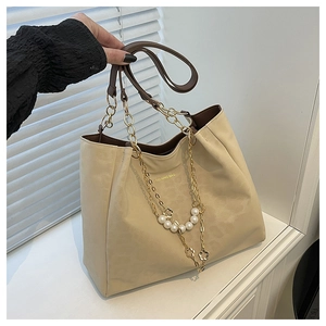 Close-up of beige tote bag with gold chain, pearls, and flower pendant charm