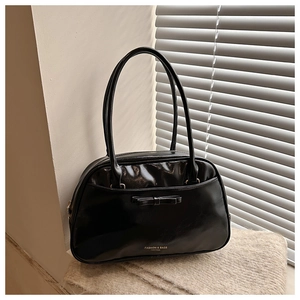 Détail du sac à bandoulière en cuir noir brillant avec un nœud et lettrage élégant