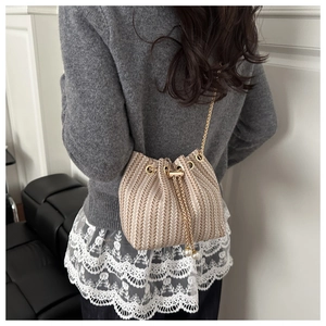 Detail view of a beige woven bucket bag with gold chain strap and pearl drawstring accents