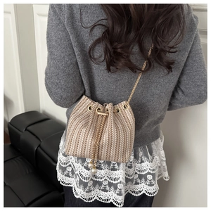 Close-up of woven bucket bag featuring V-shaped texture, gold chain and pearl drawstring