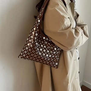 Sac hobo marron clouté en cuir brillant porté avec un trench-coat kaki style gothique