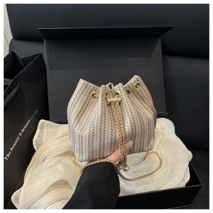 Detail view of woven bucket bag with chevron patterns, chain strap and pearl drawstring charms