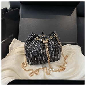 Detail of herringbone bucket bag with gold chain strap and pearl accents on silk