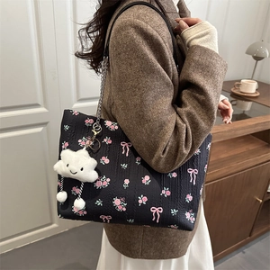 Floral black tote bag with pink bow pattern and plush charm shown on a model