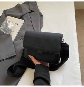 Detail of minimalist matte black square bag with wide fabric strap and fashion logo