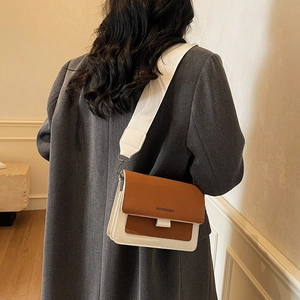 Brown and white leather crossbody bag with wide shoulder strap and modern flap design