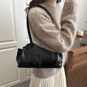 Borsa baguette nera lucida con spalline lunghe indossata da modella in interno sobrio