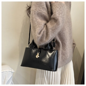 Détail d'un sac à main en similicuir noir brillant avec fermoir doré sur un mannequin