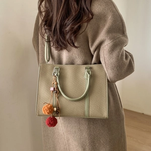Sac fourre-tout tressé vert sauge avec pendentif porté sur un manteau en cachemire
