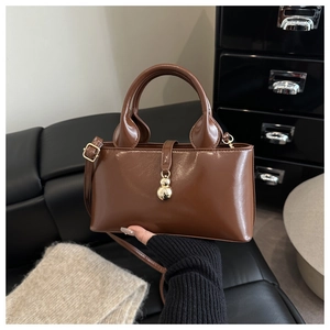 Détail du sac seau en cuir marron foncé avec un pendentif décoratif en or