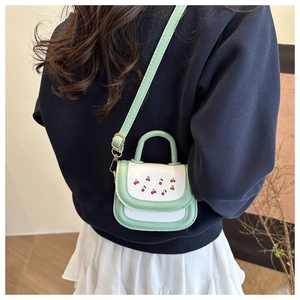 Chic mint green mini square bag with cherry print worn over a casual blue sweatshirt