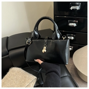 Détail d'un sac à main noir brillant avec un pendentif boule dorée et une fine bandoulière