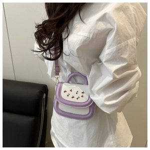 Detail of a purple and cream leather crossbody bag featuring red cherry prints