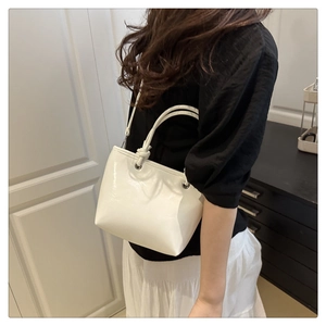 Détail du sac seau en cuir verni blanc avec poignée nouée et détails d'oeillets