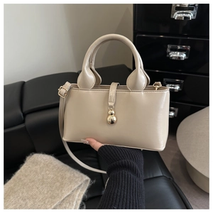 Détail d'un sac seau en cuir beige avec breloque dorée et fine bandoulière