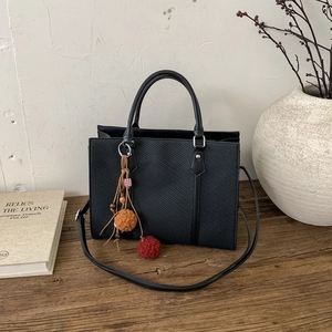 Detail of black textured tote bag with colorful plush charm on a wooden surface