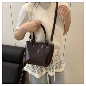Détail du sac seau en cuir verni marron foncé avec fini brillant et fine bandoulière