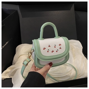 Detail of mint green and white crossbody bag with cherry pattern on silk background