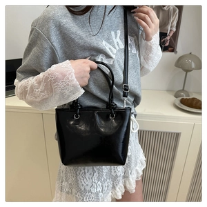 Détail du sac seau noir brillant avec poignées rondes et finitions métalliques argentées