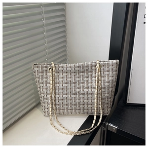 Detail of tweed tote bag with woven texture, leather chain strap and metal eyelets