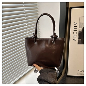 Gros plan d'un sac seau en cuir brillant marron foncé avec poignées nouées et anneau en métal