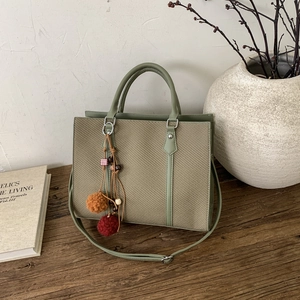 Detail of avocado green woven tote bag with fringe charm and smooth leather handles