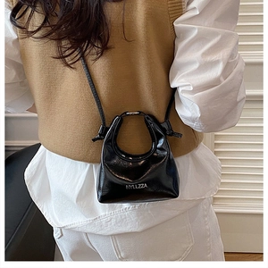 Detail of black glossy patent leather crossbody bag showing handle and shoulder strap