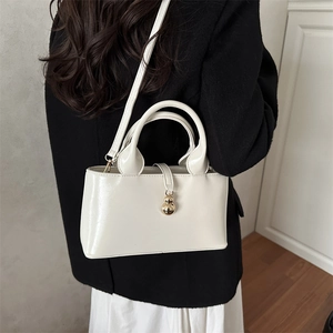 Sac seau minimaliste blanc crème avec pendentif doré vu sous un angle latéral