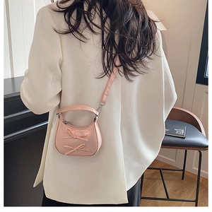 Gros plan d'un mini sac demi-lune rose avec nœuds, porté sur un blazer blanc par un mannequin