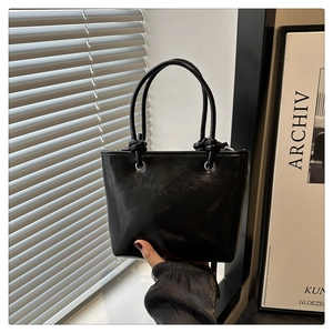 Détail d'un sac seau en cuir noir brillant avec poignée nouée et œillets argentés polis