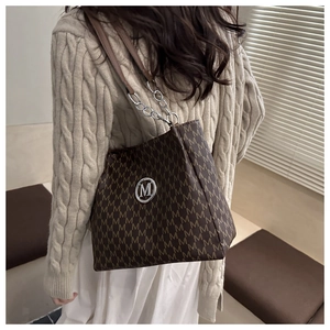 Close-up of brown tote bag with M-letter pattern and metal chain leather strap