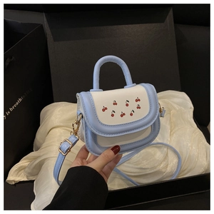 Detail of a mini white and blue crossbody bag with cherry print in a gift box