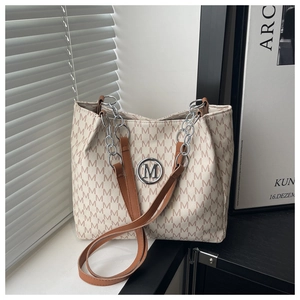 Close-up of beige tote bag featuring M-letter print and metallic M logo with silver chain