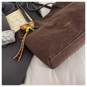 Detailed close-up of a vintage brown tote bag with contrast stitching and plush bear charm